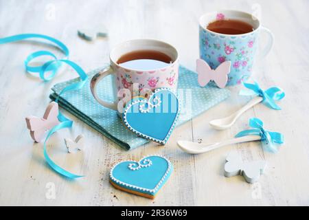 Des biscuits en forme de cœur décoré de glaçage blanc et bleu et servi avec deux tasses de thé Banque D'Images