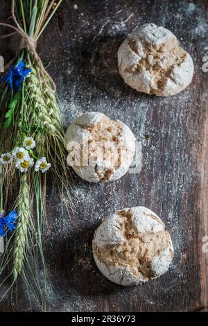 Des petits pains complet sains avec des oreilles d'avoine et des fleurs de champ sur une planche de bois Banque D'Images