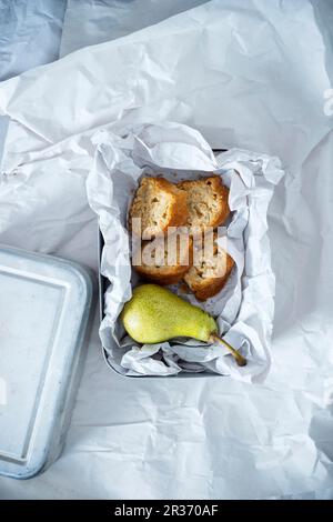 Une boîte à lunch contenant une poire et quatre morceaux de poire vegan gâteau d'épeautre et de maïzena, édulcoré avec du sucre de coco blossom Banque D'Images