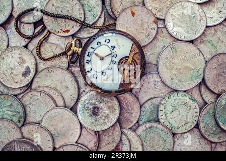 Un bouquet de vieilles pièces de monnaie argentées avec une montre de poche cassée sur le dessus Banque D'Images