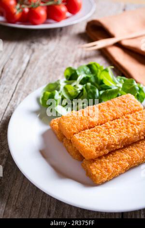 Bâtonnets de poisson frits avec salade et tomates dans une assiette sur la table en bois Banque D'Images