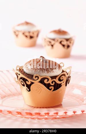 Un cupcake au chocolat de la nourriture du diable sur une assiette rose avec deux autres en arrière-plan sur un tissu rose clair Banque D'Images