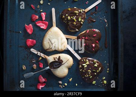 Gâteaux végétaliens en forme de coeur sur bâtonnets, décorés d'un glaçage à la bière foncée, de fraises lyophilisées et de pistaches Banque D'Images