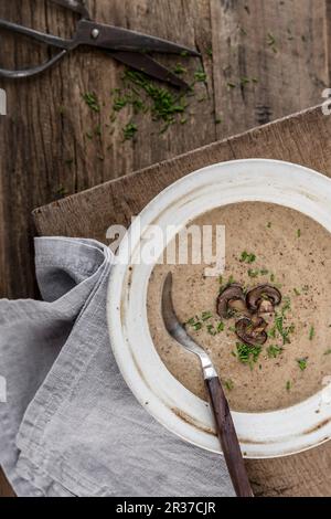 Soupe de champignons épaisse et crémeuse garnie de tranches de champignons et de ciboulette dans un bol blanc sur une surface en bois Banque D'Images