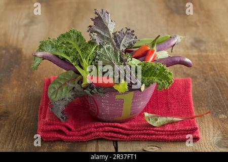 Un bol à légumes contenant du chou vert, des piments et des aubergines longues et fines Banque D'Images