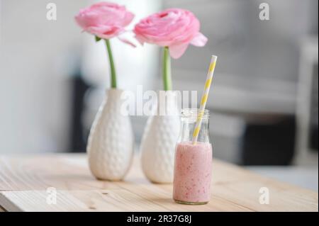 Lait de framboise avec une paille en bouteille et fleurs de ranunculus roses en deux vases Banque D'Images