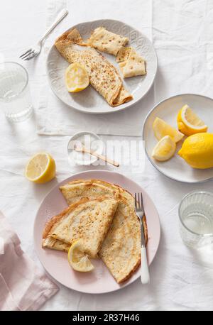 Deux plaques de plié et crêpes roulées avec des quartiers de citron sur des draps blancs couverts table et verres à eau Banque D'Images