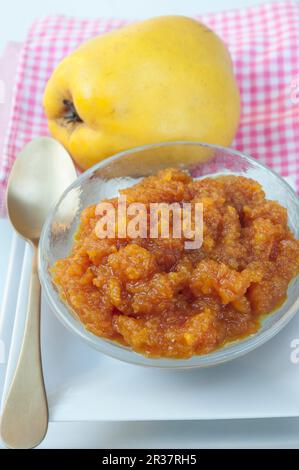 Gros plan de la confiture de coings (Cydonia oblonga) dans un plat rond en verre avec une cuillère d'or et un coing frais avec une serviette rose Banque D'Images