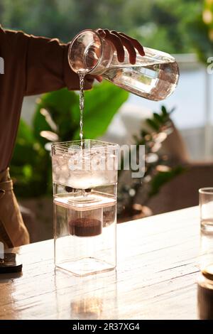 Le barista verse de l'eau fraîche dans la cafetière à filtre froid Banque D'Images