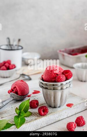 Sorbet framboise dans des bols en métal avec une cuillère à glace sur une planche en bois Banque D'Images