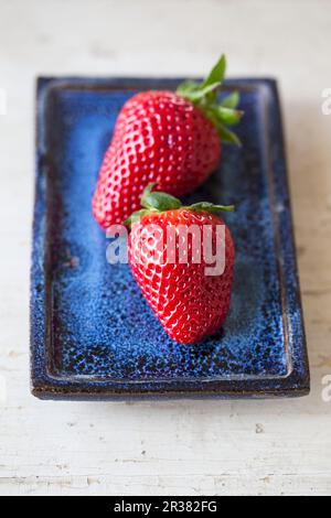 Deux fraises sur une assiette bleue Banque D'Images