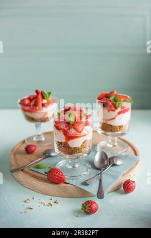 Cheesecakes à la fraise et à la vanille avec une base de biscuits aux noix servies dans de petits verres Banque D'Images