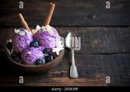 Boules de glace à la myrtille surmonté d'amandes effilées et le chocolat gaufre bobines dans un bol en bois Banque D'Images