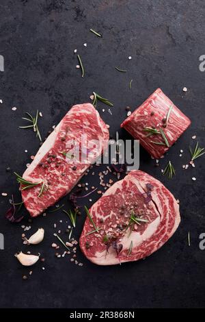 Divers steaks de bœuf aux herbes et aux épices sur fond noir Banque D'Images