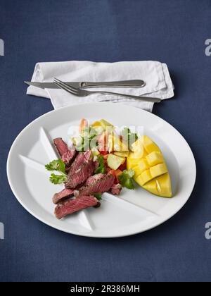 Entrecote grillé avec une salade de papaye, de mangue, de concombre, de tomates et de vert coriandre Banque D'Images