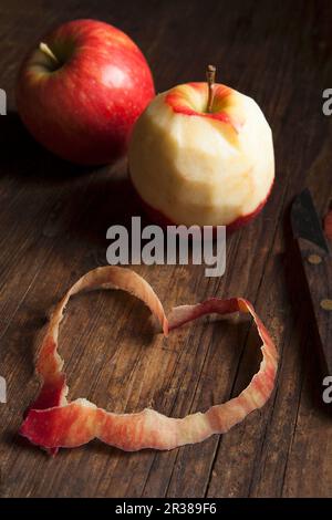Deux pommes entières, une pelée, et un coeur fait des pelures Banque D'Images