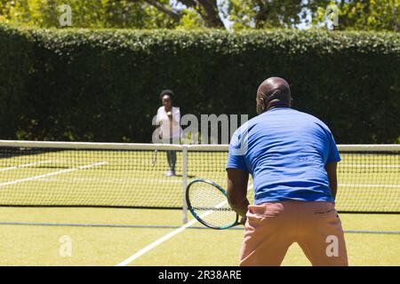 Joyeux couple afro-américain senior jouant au tennis sur un court de tennis en herbe ensoleillé Banque D'Images