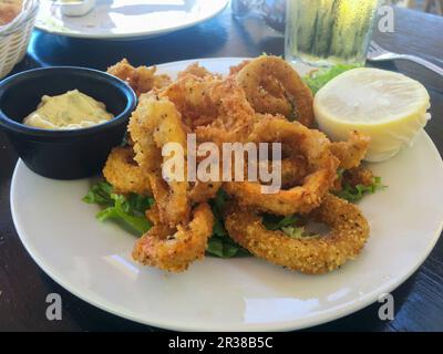 Une portion de calamars frits est servie sur une assiette blanche avec un citron et une sauce trempée Banque D'Images