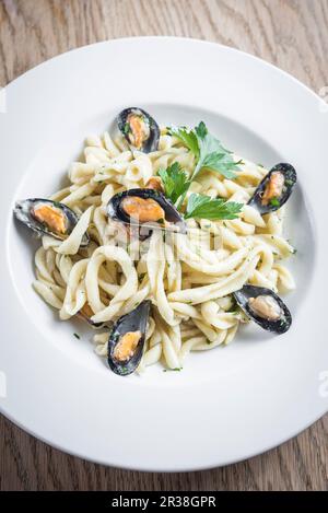 Pâtes fraîches artisanales traditionnelles avec moules et sauce crémeuse au fromage pecorino, garnies de persil dans une assiette blanche Banque D'Images