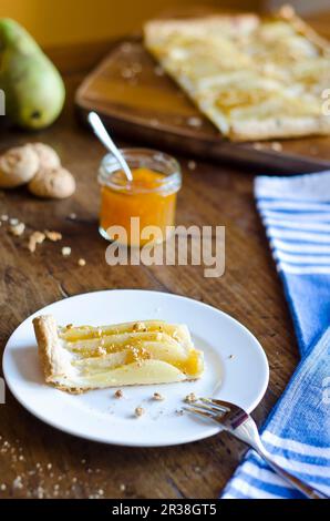 Tarte sucrée maison avec confiture de pêche, poires et chapelure d'amaretti sur une assiette blanche sur un fond rustique en bois avec serviette bleue et fourchette Banque D'Images