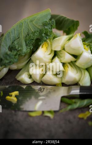 Bok choy coupé en quartiers, avec un couteau sur une planche à découper en bois Banque D'Images