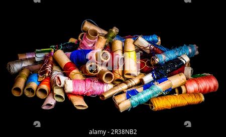 Pile de bobines colorées utilisées de fil de tailleur, sur fond noir Banque D'Images