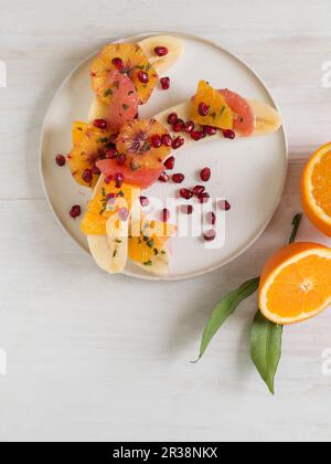 Bananes coupées en deux avec des oranges, des pamplemousses et des graines de grenade Banque D'Images