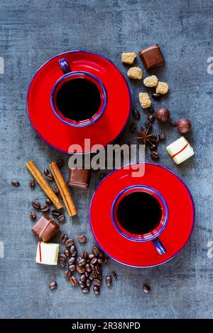 Composition de café avec deux tasses rouges, épices et chocolat sur fond vintage sombre Banque D'Images