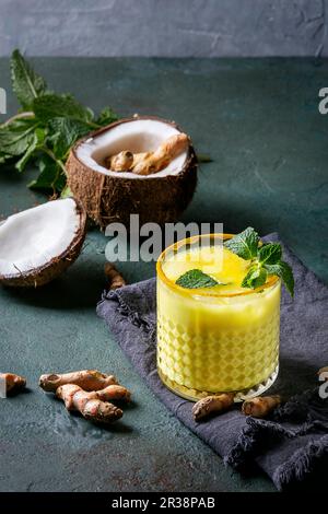 Verre de boisson ayurvédique lait de coco doré latte glacée au curcuma, poudre, menthe et ingrédients Banque D'Images