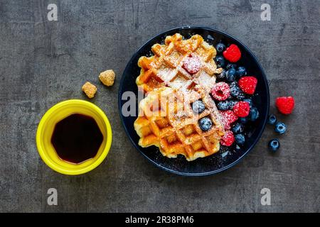 Gaufres belges faites maison avec baies sur une assiette noire, tasse à expresso et cubes de sucre brun Banque D'Images