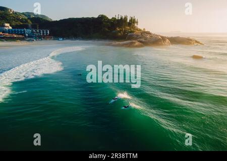 Lever de soleil chaud sur l'océan avec les surfeurs sur la vague. Plage de Joaquina au Brésil Banque D'Images
