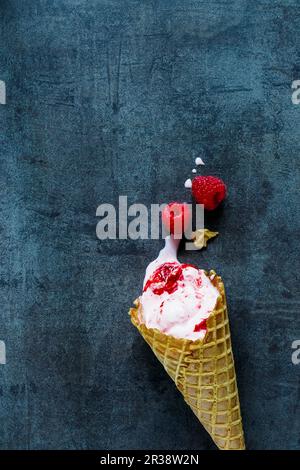 Crème glacée à la framboise dans un cône sur une surface gris bleu (vue de dessus) Banque D'Images