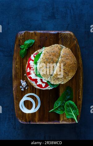 Sandwich végétarien sain avec feta, tomates, basilic et poivre servi sur une planche à découper en bois sur fond vintage Banque D'Images