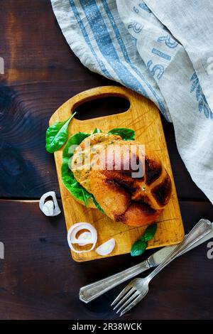 Vue de dessus du poisson frais et du hamburger de crabe avec des tranches d'oignon sur une petite planche à découper en bois sur fond rustique sombre Banque D'Images