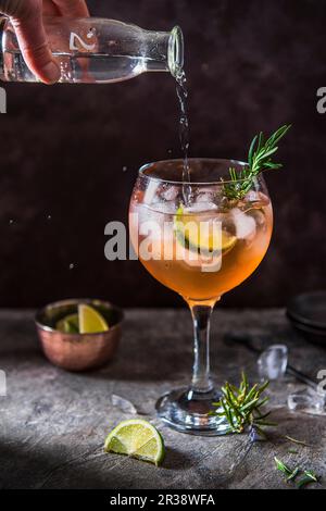 Cocktail de gin rose avec amers d'angostura, citron vert et romarin, verser de l'eau tonique Banque D'Images