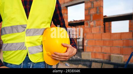 Travailleur de la construction dans la zone du site. Travailleur dans une veste jaune tenant un casque de sécurité et restant devant la zone du bâtiment. Travailleur de la construction sur le travail zo Banque D'Images