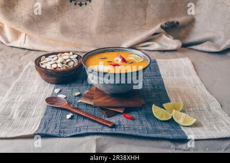 Soupe de potiron asiatique épicée aux piments rouges, aux limes et aux graines de potiron, nappée de crème de noix de coco Banque D'Images