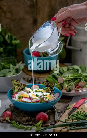 Vinaigrette versée sur une salade avec des radis et des œufs durs Banque D'Images
