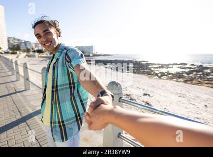 Heureux biracial gay couple mâle tenant les mains sur la promenade ensoleillée au bord de la mer Banque D'Images