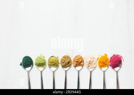 Ustensiles de cuisine avec différentes poudres de superalimentaire colorées sur table en bois Banque D'Images