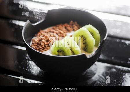 Yaourt avec granola et kiwi dans un bol noir Banque D'Images