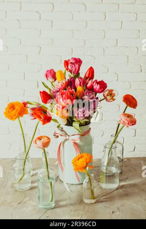 Bouteilles en verre avec fleurs de ranunculus autour d'un vase avec tulipes Banque D'Images