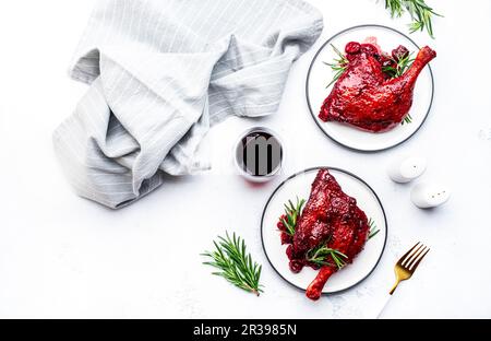 Pattes de canard cuites dans une sauce à la cerise et au vin avec du romarin frais. Dîner gastronomique. Arrière-plan de table blanc, vue du dessus Banque D'Images