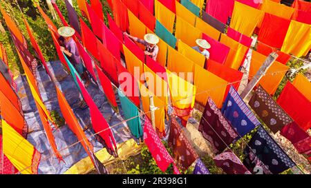 Narayanganj, Dhaka, Bangladesh. 23 mai 2023, Narayanganj, Dhaka, Bangladesh : les travailleurs pendent des centaines de feuilles de tissu colorées sur un cadre en bambou pour sécher dans une usine de teinture à Narayanganj, au Bangladesh. Le processus de séchage prend généralement 4 heures, chaque ensemble de 200 pièces à la fois pour sécher à des températures supérieures à 42 degrés Celsius. Les travailleurs utilisent des chapeaux pour se protéger de la chaleur brûlant parce qu'ils doivent constamment tourner les tissus colorés pour qu'ils sèchent parfaitement au soleil. Crédit : ZUMA Press, Inc./Alay Live News Banque D'Images