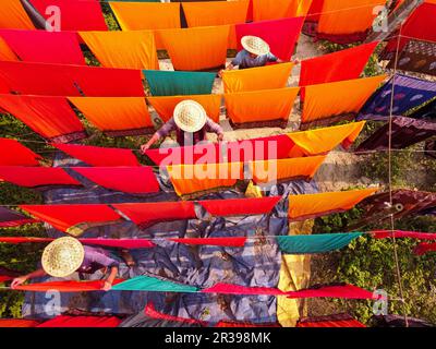 Narayanganj, Dhaka, Bangladesh. 23 mai 2023, Narayanganj, Dhaka, Bangladesh : les travailleurs pendent des centaines de feuilles de tissu colorées sur un cadre en bambou pour sécher dans une usine de teinture à Narayanganj, au Bangladesh. Le processus de séchage prend généralement 4 heures, chaque ensemble de 200 pièces à la fois pour sécher à des températures supérieures à 42 degrés Celsius. Les travailleurs utilisent des chapeaux pour se protéger de la chaleur brûlant parce qu'ils doivent constamment tourner les tissus colorés pour qu'ils sèchent parfaitement au soleil. Crédit : ZUMA Press, Inc./Alay Live News Banque D'Images