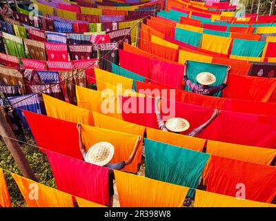 Narayanganj, Dhaka, Bangladesh. 23 mai 2023, Narayanganj, Dhaka, Bangladesh : les travailleurs pendent des centaines de feuilles de tissu colorées sur un cadre en bambou pour sécher dans une usine de teinture à Narayanganj, au Bangladesh. Le processus de séchage prend généralement 4 heures, chaque ensemble de 200 pièces à la fois pour sécher à des températures supérieures à 42 degrés Celsius. Les travailleurs utilisent des chapeaux pour se protéger de la chaleur brûlant parce qu'ils doivent constamment tourner les tissus colorés pour qu'ils sèchent parfaitement au soleil. Crédit : ZUMA Press, Inc./Alay Live News Banque D'Images