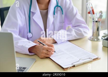 Mains du médecin généraliste remplissant les dossiers médicaux papier Banque D'Images