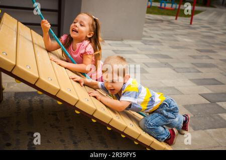 Les enfants qui essayent d'escalader la corde sur le terrain de jeux Banque D'Images