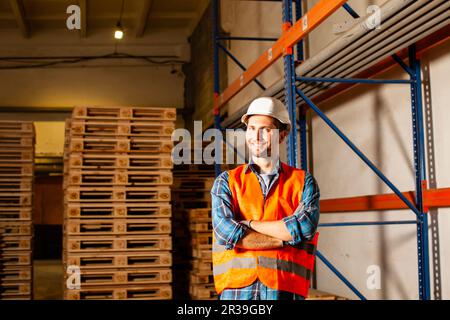 Jeune travailleur heureux en uniforme de protection devant des palettes en bois Banque D'Images