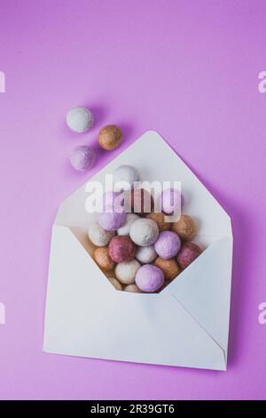 Enveloppe ouverte avec boules de feutre colorées sur fond violet. Style minimaliste. Banque D'Images